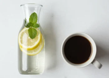 A flat-lay assortment of seven healthy drink alternatives to water, including infused water, sparkling water, green tea, black coffee, kombucha, coconut water, and a low-calorie cocktail, arranged on a marble background.