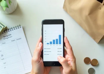 Hands using a smartphone savings app with a shopping list and cash, illustrating smart shopping strategies to save money.