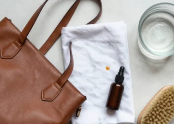 Professional flat lay of leather bag cleaning supplies: a leather handbag, conditioner, soft cloth, brush, and soapy water for home cleaning.