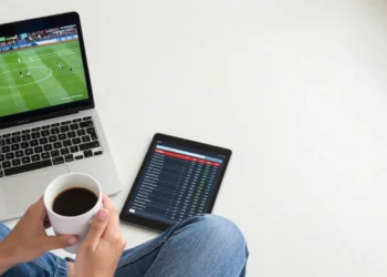 Person watching live NFL and NBA games on laptop and tablet while checking free sports news site for betting picks and predictions