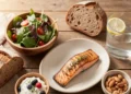 Balanced diet guide featuring salmon, Greek yogurt with berries, mixed green salad, whole grain bread, and nuts arranged on wooden table with natural lighting