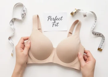 Woman's hands holding a beige t-shirt bra with a measuring tape beside it, illustrating common bra buying mistakes and how to find the right fit.