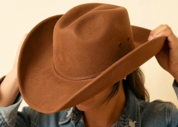 Person adjusting the fit of a brown felt cowboy hat on head showing proper western hat fit guide