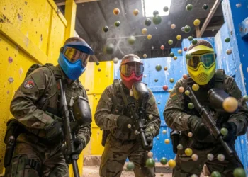 How to play paintball beginners guide - players in protective masks and gear moving between bunkers on a sunny paintball field